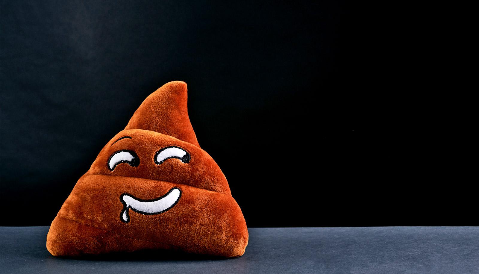 A stuffed toy of a poop emoji smiles slyly against a dark background