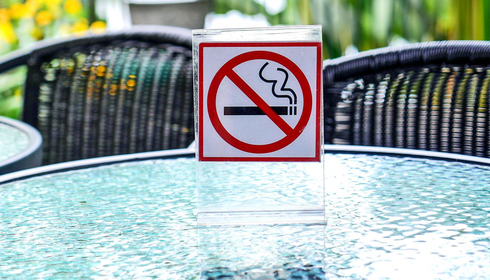 A no smoking sign sits on a glass table at an outdoor cafe