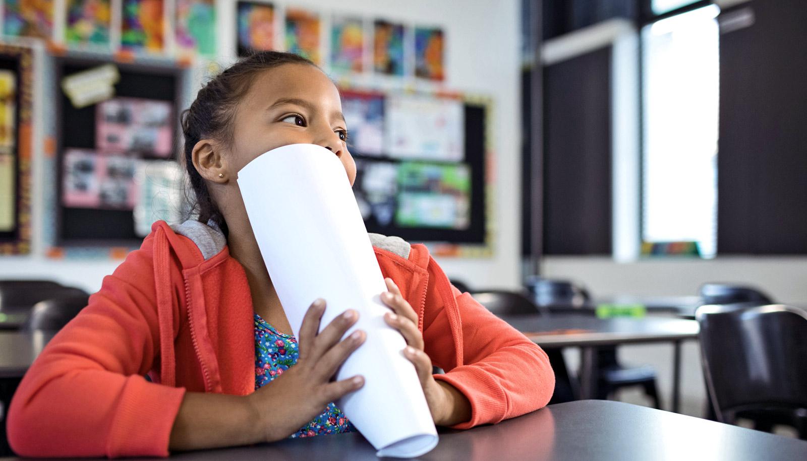 girl in classroom with papers over mouth