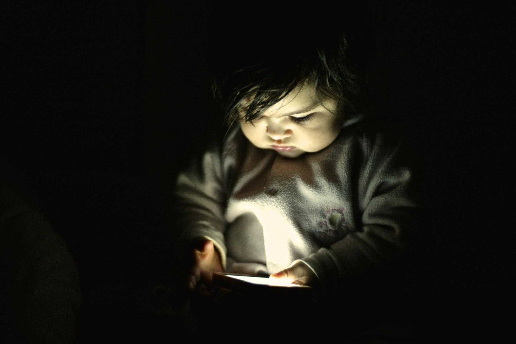 A 10-month-old baby girl looks at a smartphone screen in a dark room. Researchers found a correlation between toddlers who had half an hour per day of smartphone exposure with those who began talking later.