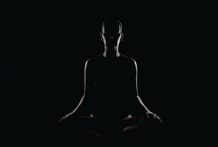 Finding Solace in Silence by Judy Marano. Photograph of a silhouette of a person meditating in the dark by Max Rovensky