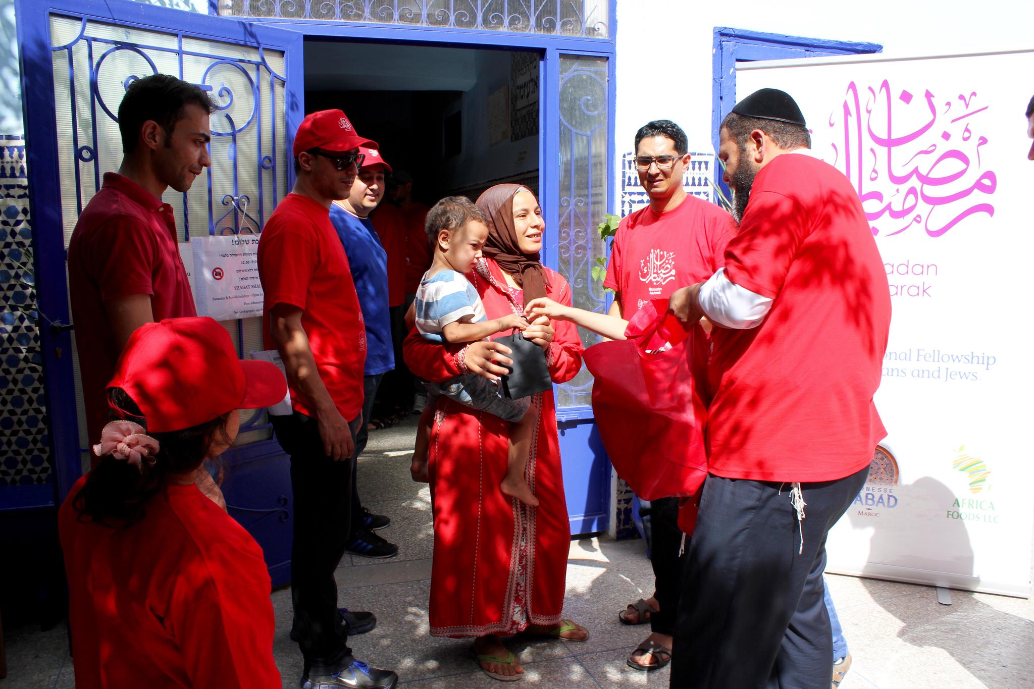 Chabad Rabbi Levi Banon hands a Ramadan meal package to a Muslim woman at a 500-year-old synagogue in the ancient Jewish quarter of Marrakesh, as Muslim members of Mimouna and Elmehdi Boudra (blue shirt), the president and co-founder of Mimouna, look on.