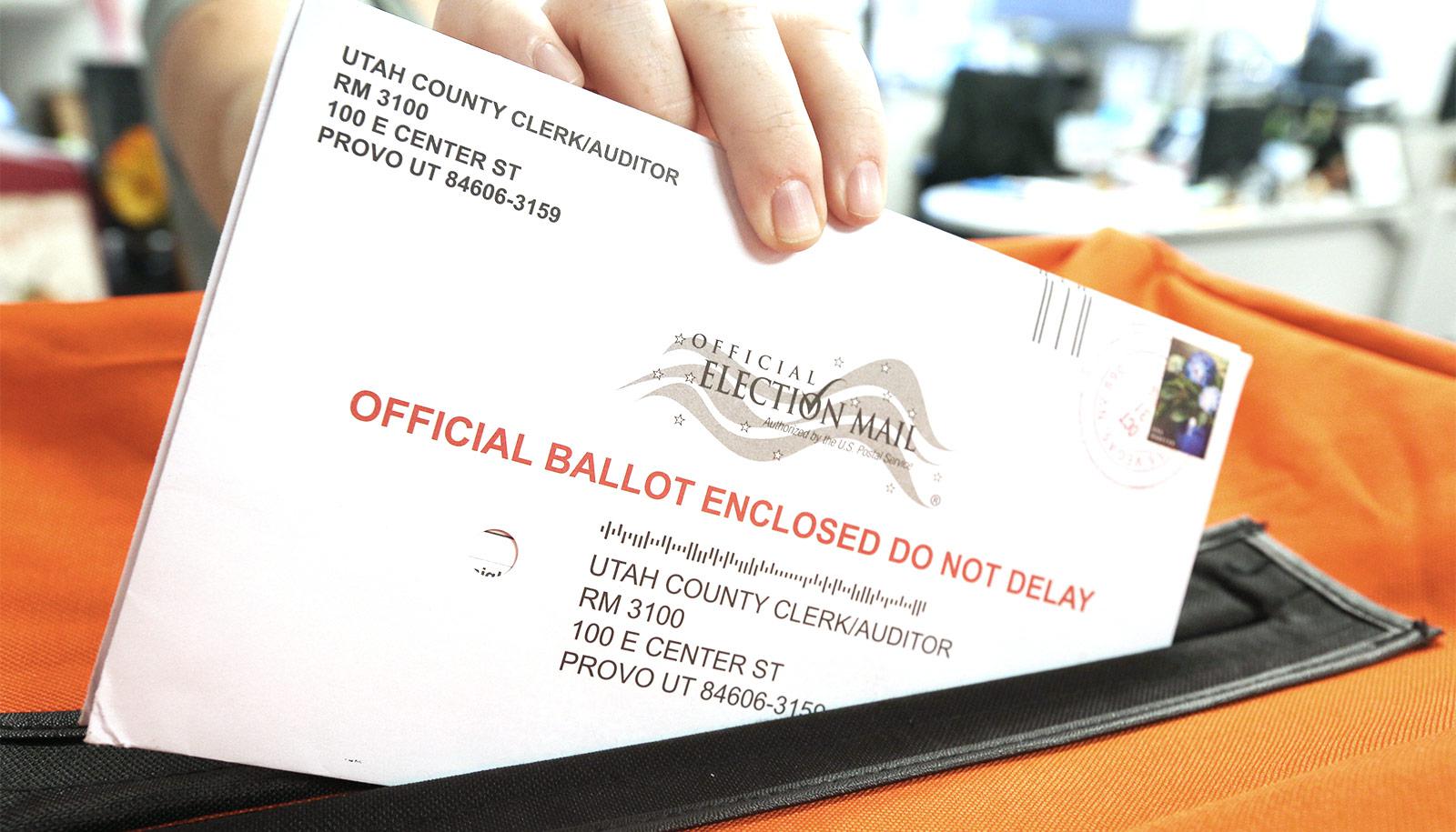 A person slides a mail-in ballot into an orange container