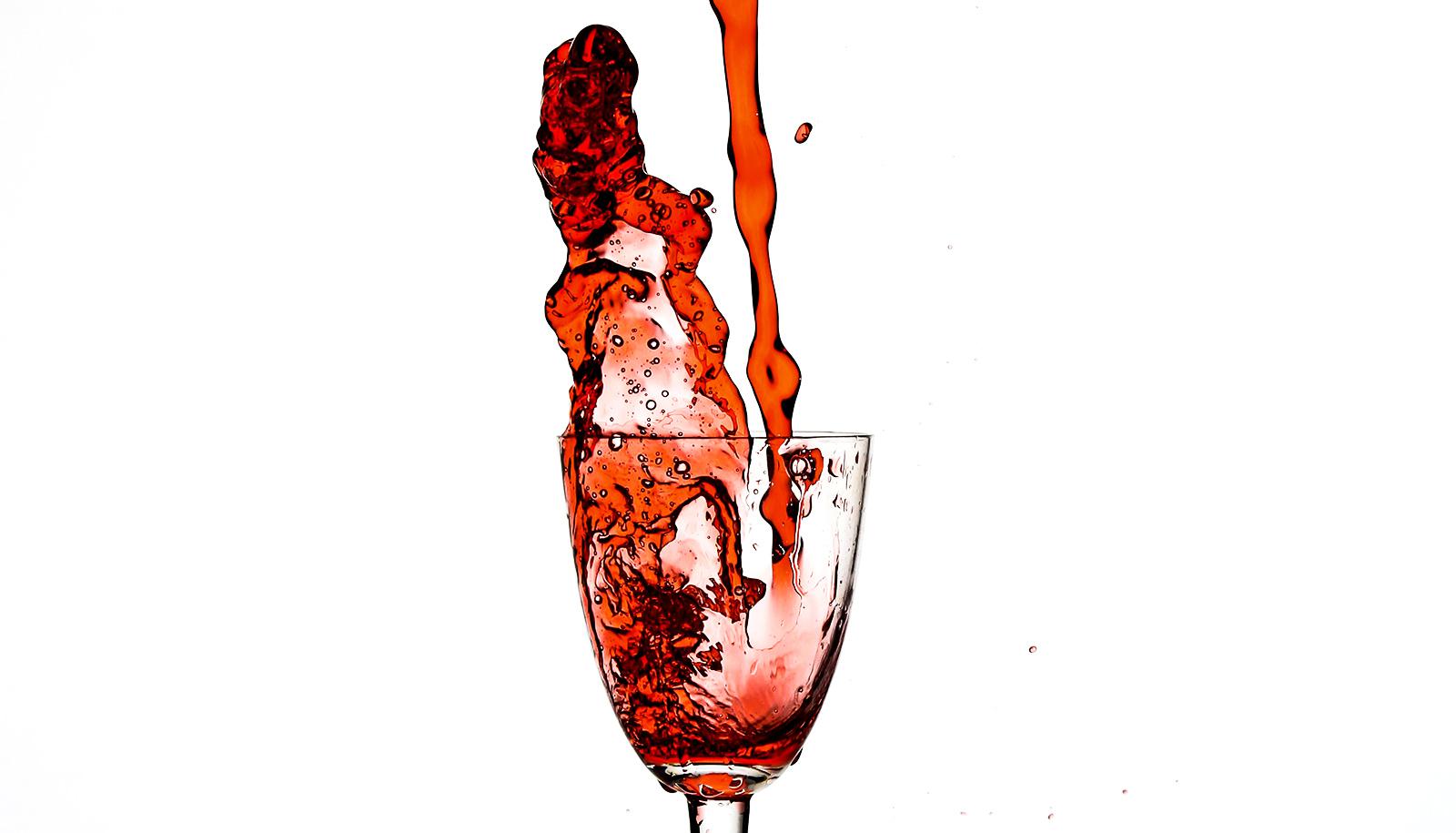 Red wine pours into a glass and then splashes out