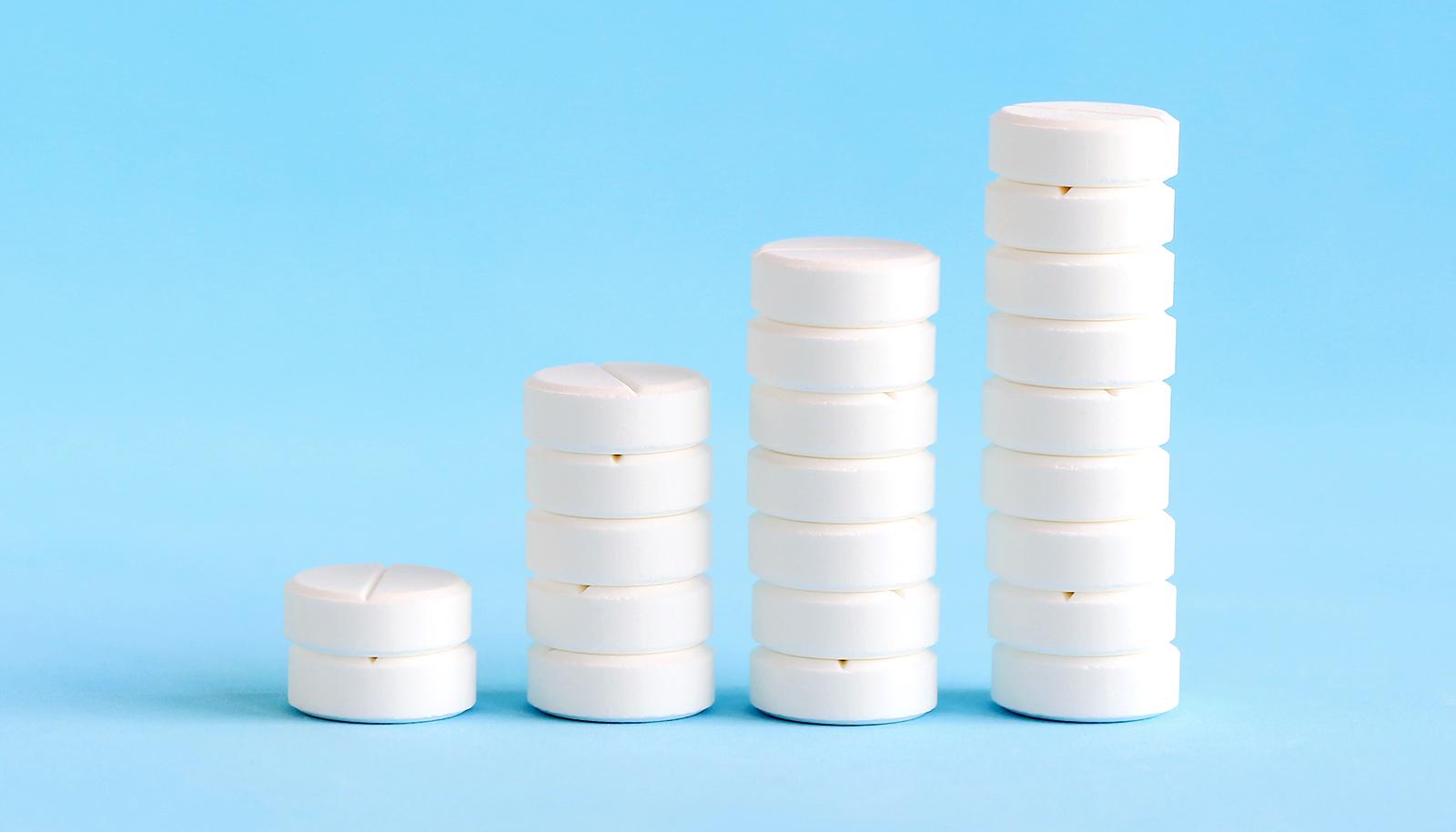 A series of stacks of white pills getting larger against a blue background