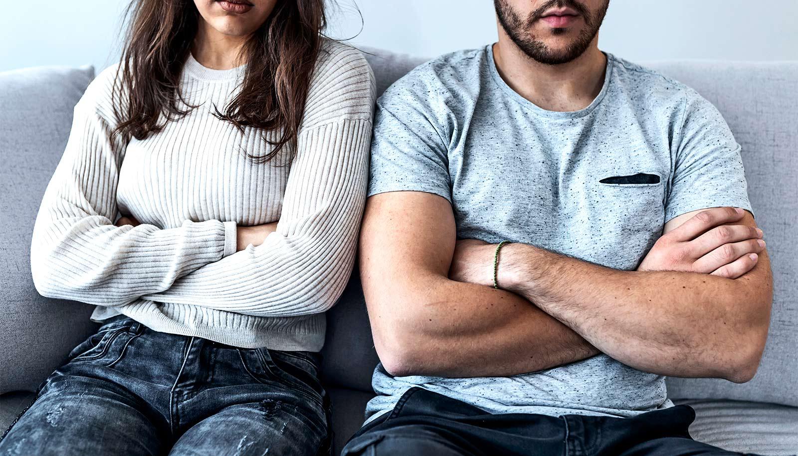 A couple sits with arms folded on a couch