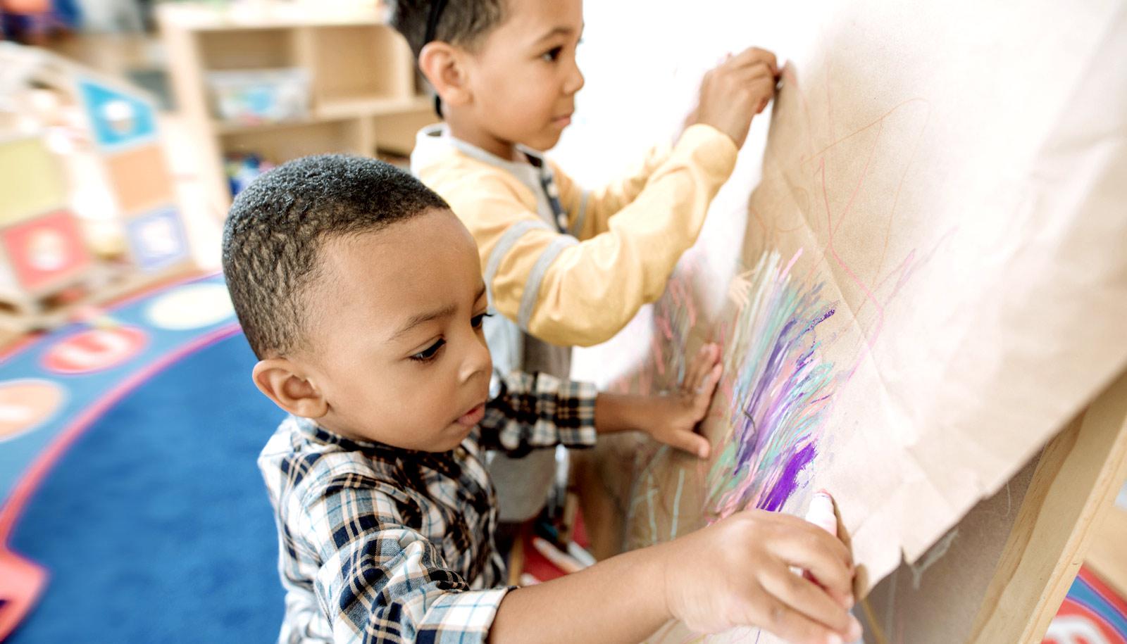 two little boys draw at easel -- early childhood education