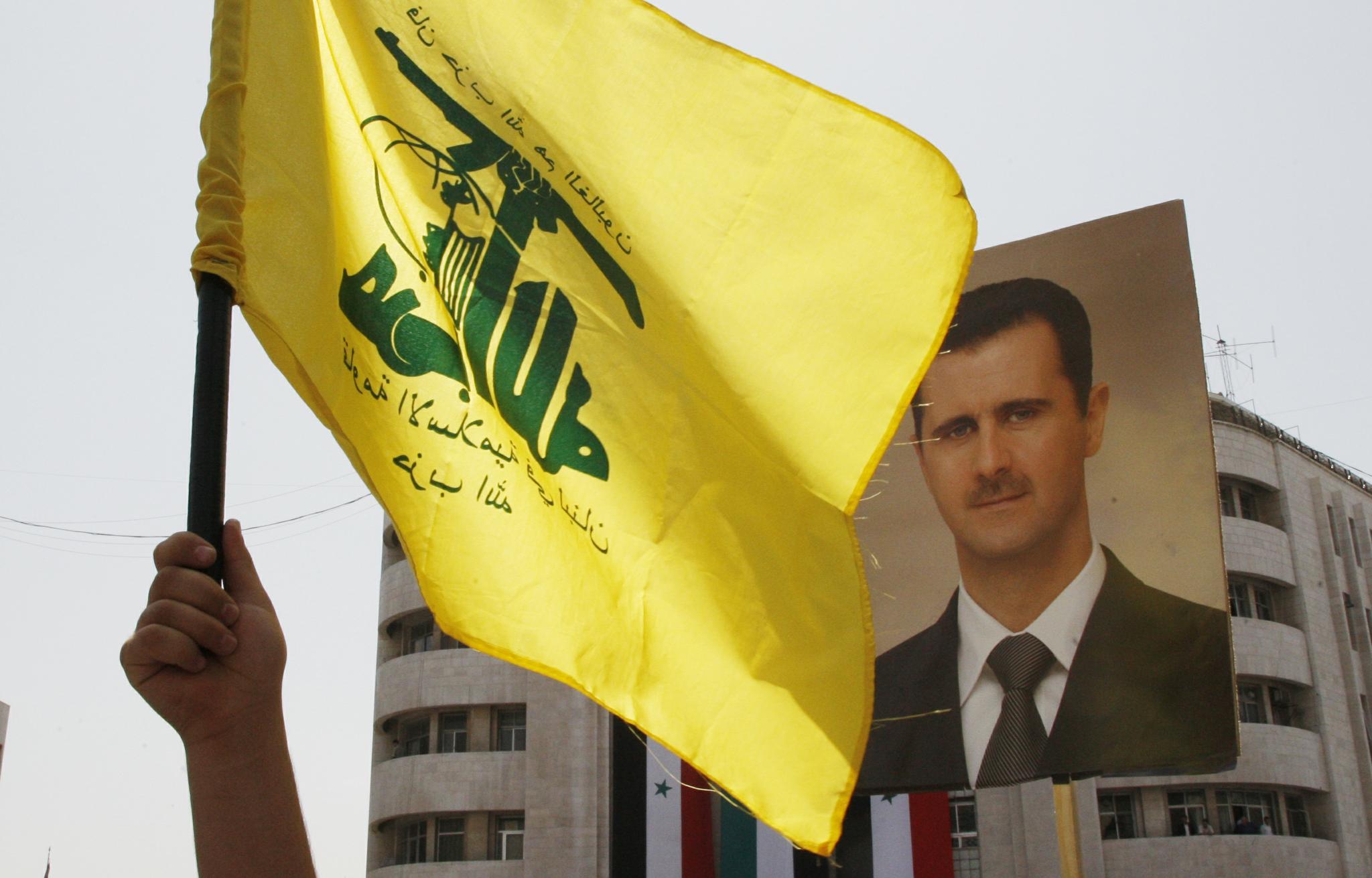 A demonstrator holds up a flag of Lebanese Hezbollah and a picture of Syrian President Bashar al-Assad during a demonstration to mark the 60th anniversary of "Nakba" in Damascus on May 15, 2008. Assad and his Syrian regime are just a figurehead in the current Syrian Civil War; the real victory belongs to Hezbollah, resurgent Party of God.