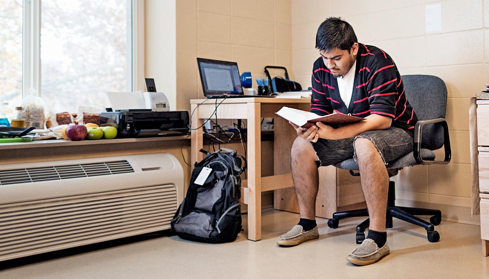 person reads book at desk in dorm room