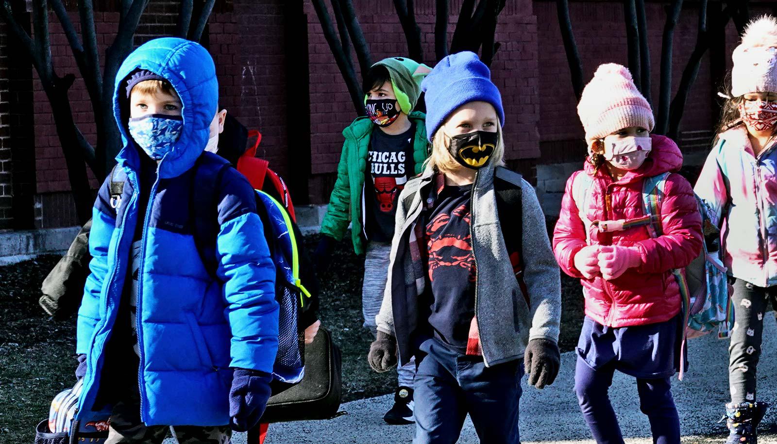 A line of schoolchildren walk with face masks and winter clothing