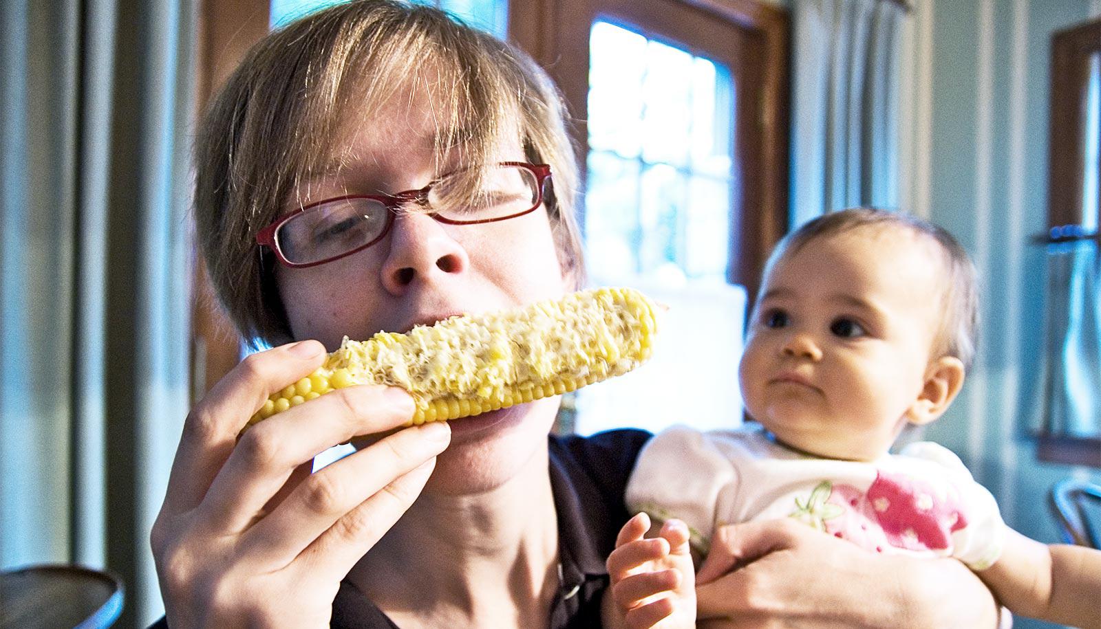 eating corn while holding baby