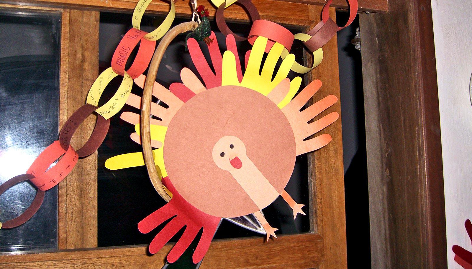 A paper turkey made with outlines of hands cut from colorful paper hangs in a doorway