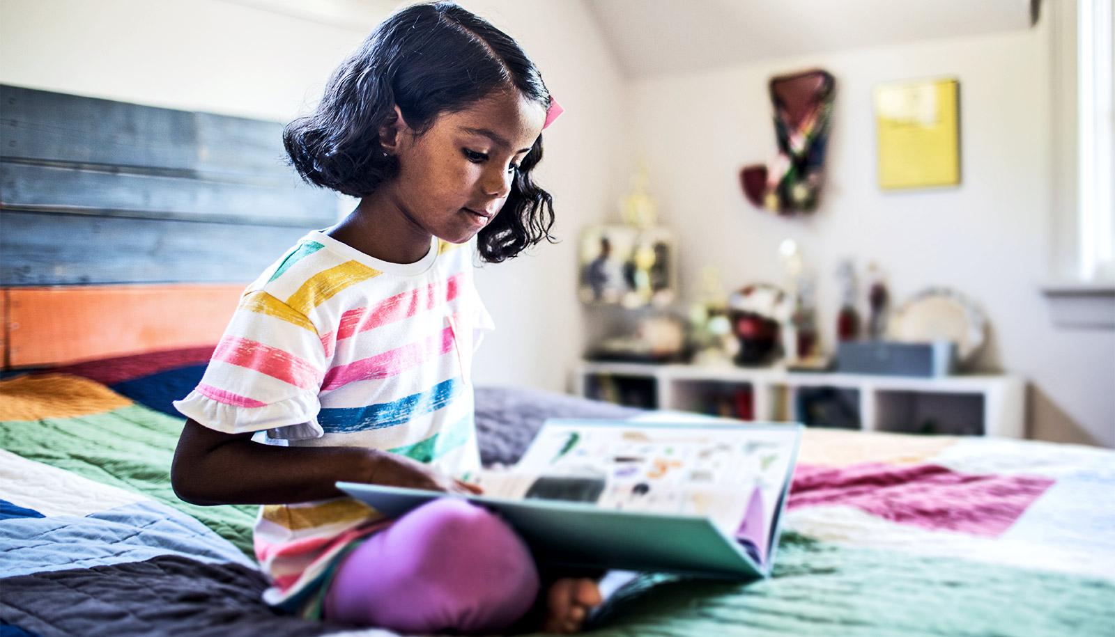 A young girl reads a book on her bed