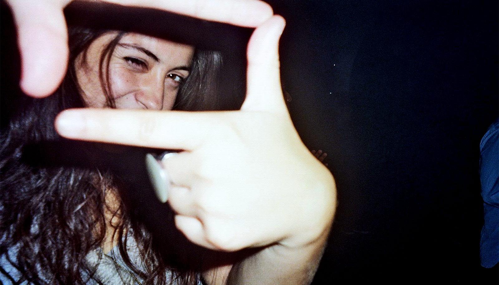 A young woman makes a "camera" with her fingers and thumbs and looks through it with one eye