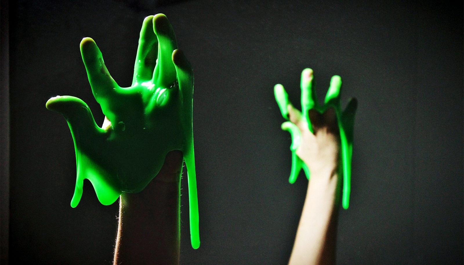 Bright green slime drips from a hand, which is also mirrored in the background