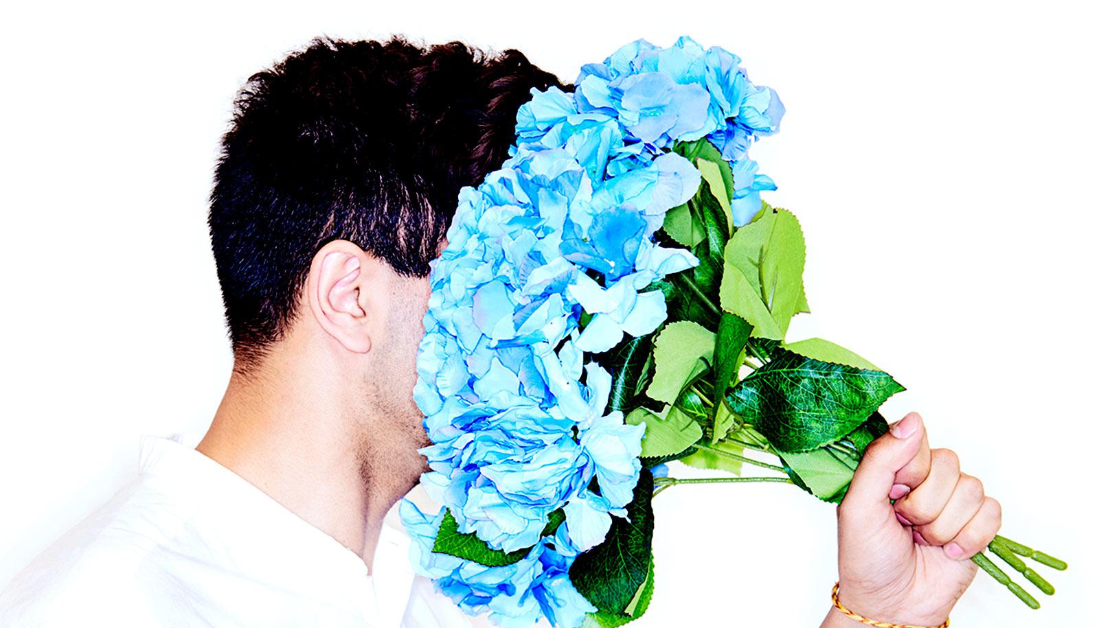 A man puts his face in a bouquet of blue flowers